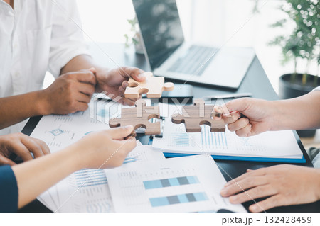 Business teamwork concept with people holding wooden puzzle pieces together, symbol of collaboration, strategy, problem solving, partnership and corporate success in modern office. business teamwork. 132428459