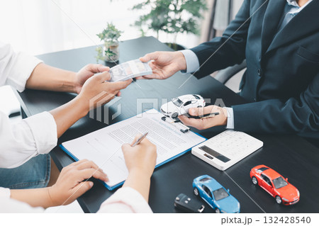 Customer paying cash to dealer with car loan contract, vehicle models on desk, concept of auto purchase, finance, leasing, insurance, successful transaction and business agreement. car loan contract 132428540