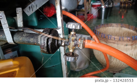 Rusty gas valve with orange hose in cluttered kitchen scene showing woven basket and containers, worn metal and pipe details evoke rustic mood Rusty gas valve with orange hose in cluttered kitchen scene showing woven basket and containers, worn metal and pipe details evoke rustic mood 132428553