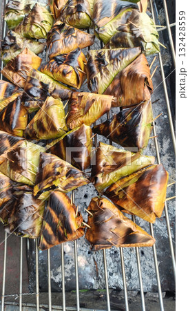 Grilled banana leaf parcels on charcoal grill, smoky savory aroma and golden charred texture evokes street food comfort 132428559