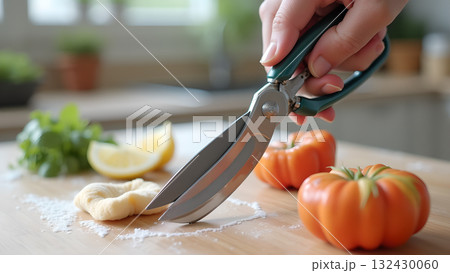 Culinary preparation featuring kitchen shears alongside tomatoes and a dough shape with lemon 132430060