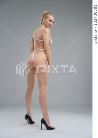 Woman poses confidently in leather belts against a simple studio background 132430681