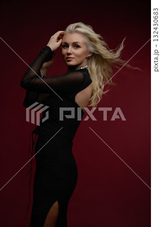 Elegant woman in black dress poses confidently against a rich burgundy backdrop Elegant woman in black dress poses confidently against a rich burgundy backdrop 132430683