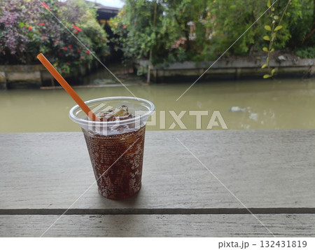 Iced drink plastic cup orange straw ice cubes wooden table river outdoor refreshing mood Iced drink plastic cup orange straw ice cubes wooden table river outdoor refreshing mood 132431819