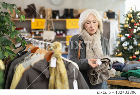 Mature woman chooses fashionable trousers for winter season in store 132432806