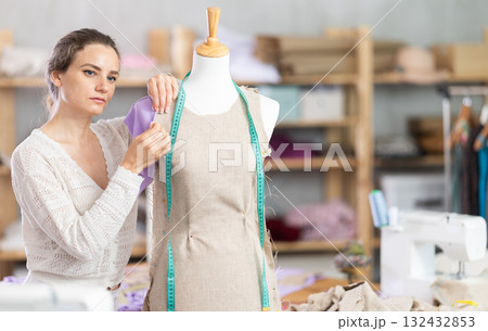 Woman tailor connects parts of dress on mannequin Woman tailor connects parts of dress on mannequin 132432853