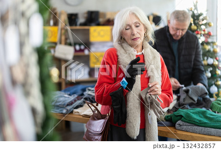 Mature woman carefully selects warm winter gloves in clothing store Mature woman carefully selects warm winter gloves in clothing store 132432857