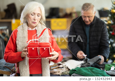 elderly woman chooses a handbag against the background of a man and a Christmas tree elderly woman chooses a handbag against the background of a man and a Christmas tree 132432943