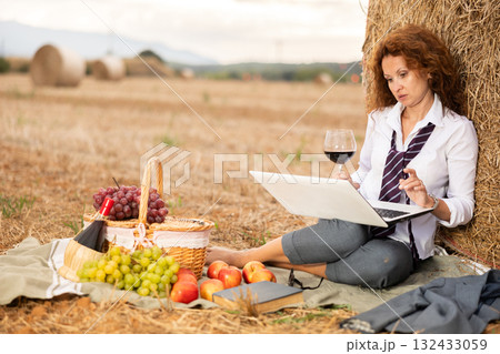 Businesswoman sipping wine and working on laptop near hay bale 132433059