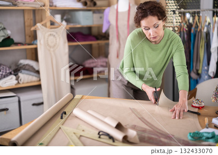 Female clothing designer cutting pattern paper in tailoring studio Female clothing designer cutting pattern paper in tailoring studio 132433070