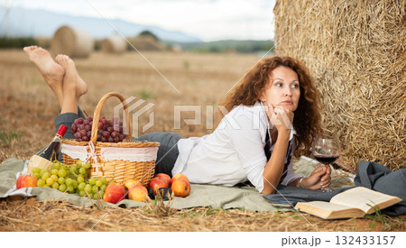 Businesswoman escaping to picnic with book and wine by hay bale 132433157