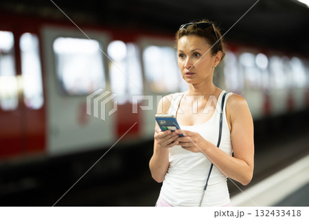 Portrait of gorgeous woman waiting for subway train with smartphone in hands at underground station Portrait of gorgeous woman waiting for subway train with smartphone in hands at underground station 132433418