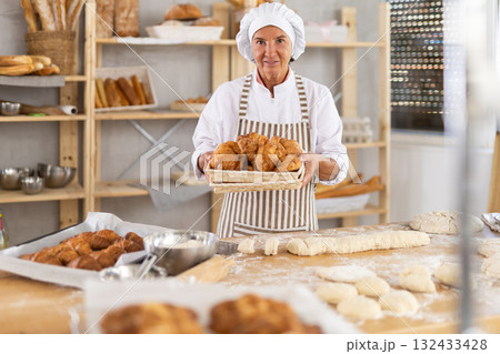 Elderly female baker with basket of croissants 132433428
