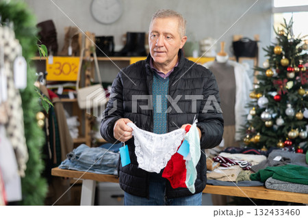 Mature male shopper selects ladies panties as a Christmas gift in fashionable clothing boutique 132433460