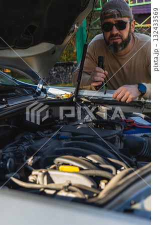 Man inspecting car engine with flashlight in outdoor setting 132433569