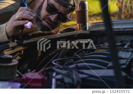 Man inspects car engine with flashlight in outdoor area Man inspects car engine with flashlight in outdoor area 132433572