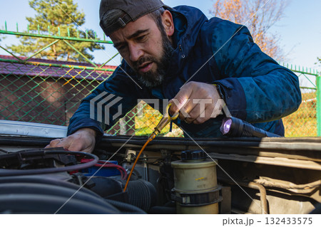 Man inspecting car engine during sunny day in a rural area Man inspecting car engine during sunny day in a rural area 132433575