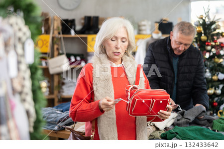 Mature woman chooses fashionable handbag in clothing boutique Mature woman chooses fashionable handbag in clothing boutique 132433642