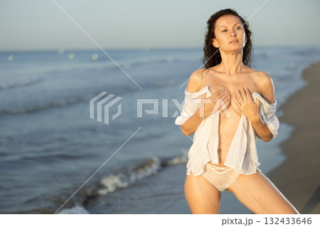 Topless woman in white shirt standing on coast 132433646