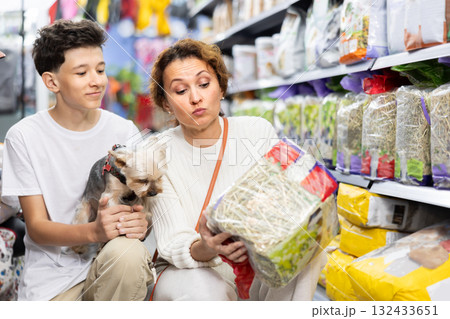 Mom and boy with dog Yorkshire Terrier, take hay from shelf, in pet store. Mom and boy with dog Yorkshire Terrier, take hay from shelf, in pet store. 132433651