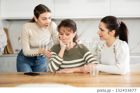 Sad middle-aged woman sitting at table while two others trying to calm her 132433677