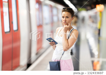 Adult woman stands at subway station with phone Adult woman stands at subway station with phone 132433697