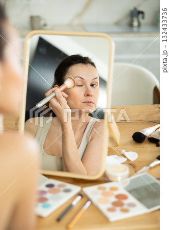 Woman applying blush with brush, reflecting in mirror 132433736