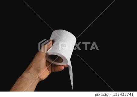 Hand holding a roll of white tissue paper against a black background 132433741