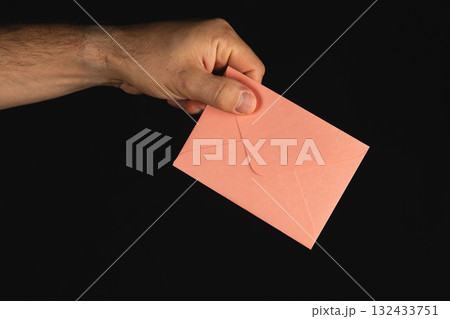 Hand holding a pink envelope in front of a dark background during evening Hand holding a pink envelope in front of a dark background during evening 132433751