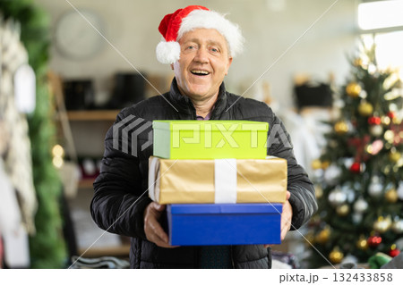 Elderly man in Santa hat with gift boxes in store Elderly man in Santa hat with gift boxes in store 132433858