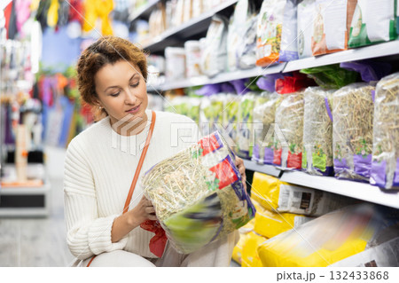 Smiling woman choosing package with dry hay in pet store Smiling woman choosing package with dry hay in pet store 132433868