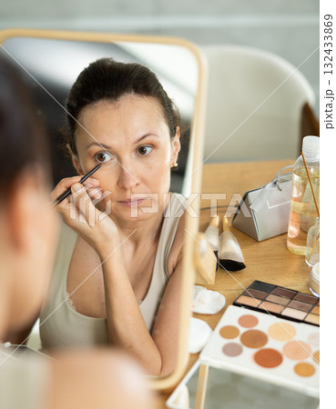 Woman drawing eyeliner wing in front of home vanity mirror 132433869