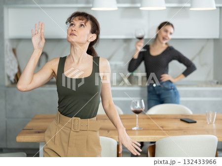 Middle-aged women dancing at the kitchen-table with wineglasses Middle-aged women dancing at the kitchen-table with wineglasses 132433966