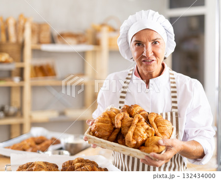 Elderly female baker with basket of croissants 132434000