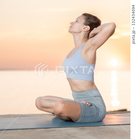 Young beautiful woman relaxing and enjoying yoga on beach at sunrise, meditation in lotus pose with hands behind head Young beautiful woman relaxing and enjoying yoga on beach at sunrise, meditation in lotus pose with hands behind head 132434094