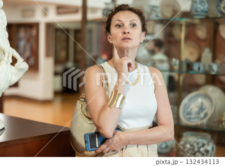 Interested woman looking at collection of medieval sculptures and objects in history museum Interested woman looking at collection of medieval sculptures and objects in history museum 132434113