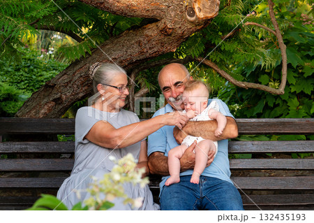 Happy elderly couple with baby granddaughter on garden bench Happy elderly couple with baby granddaughter on garden bench 132435193