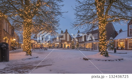 Snow-covered village square with Christmas lights on trees . Snow-covered village square with Christmas lights on trees . 132436725
