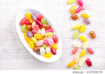 Jelly beans, flavor and color assortment, in oval white bowl, on linen. Small bean-shaped sugar candies with soft candy shells and thick gel interiors, in a wide variety of colors and flavors. Photo Jelly beans, flavor and color assortment, in oval white bowl, on linen. Small bean-shaped sugar candies with soft candy shells and thick gel interiors, in a wide variety of colors and flavors. Photo 132438159
