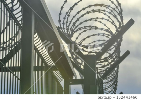 Barbed wire on a high-security building. Barbed wire and solid wire fencing. Concepts for detention centers, military facilities, nuclear power plants, and defense against illegal migration. Barbed wire on a high-security building. Barbed wire and solid wire fencing. Concepts for detention centers, military facilities, nuclear power plants, and defense against illegal migration. 132441460