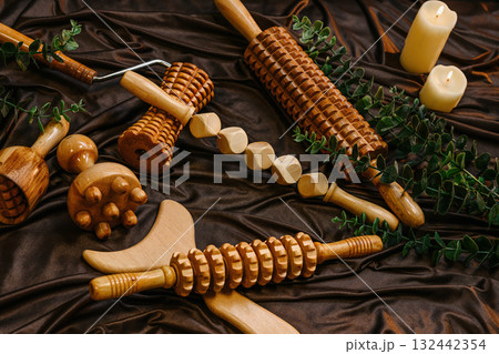 Set of wooden massage tools for body therapy and relaxation on brown silk fabric with candle Set of wooden massage tools for body therapy and relaxation on brown silk fabric with candle 132442354