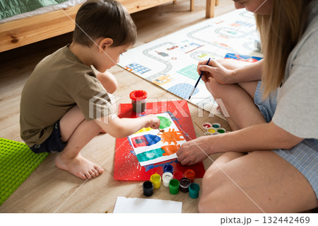 Child painting with mother in creative indoor space with colorful materials 132442469