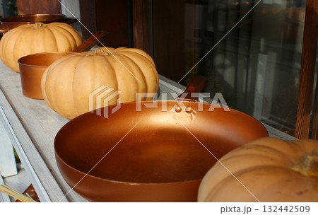 A shelf at a country fair adorned with vintage copper cooking utensils nestled between ripe pumpkins 132442509
