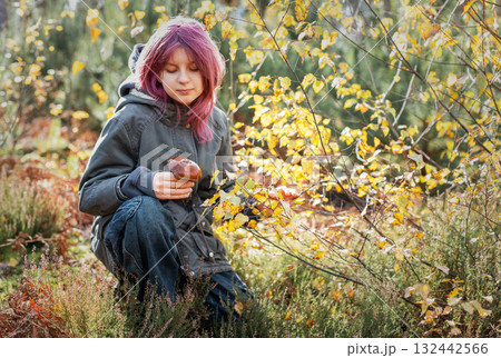 Girl with pink hair foraging mushrooms in autumn forest 132442566