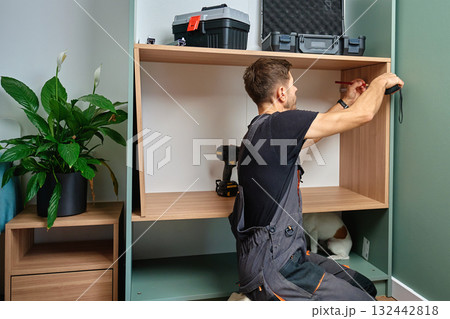 Man measuring wooden cabinet, using measuring tape and pencil to mark panel during home furniture assembly 132442818