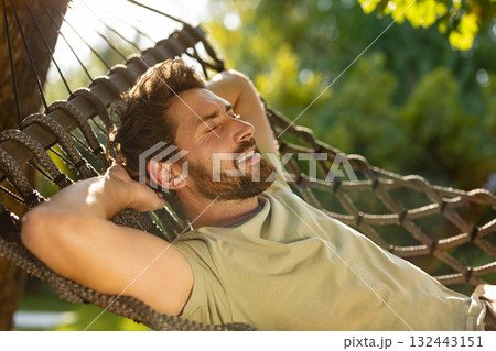 Bearded young man lying in a hammock and feeling relaxed Bearded young man lying in a hammock and feeling relaxed 132443151