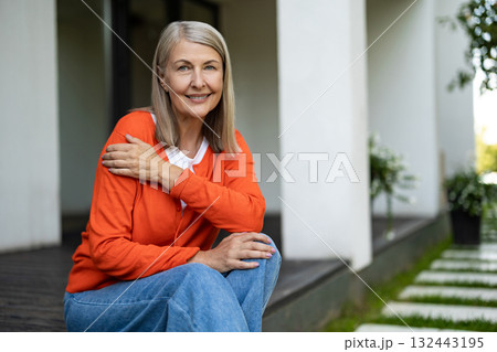 Senior good-looking woman sitting on the steps of her house and feeling contented Senior good-looking woman sitting on the steps of her house and feeling contented 132443195