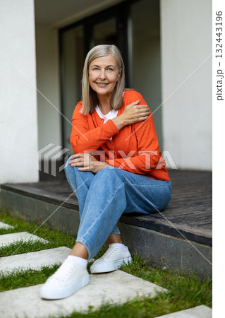 Senior good-looking woman sitting on the steps of her house and feeling contented 132443196