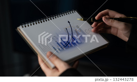 Business professional analyzing data trends with a pen on graph visuals in a notebook, focusing on growth indicators and statistics, finance analysis Scalp Business professional analyzing data trends with a pen on graph visuals in a notebook, focusing on growth indicators and statistics, finance analysis Scalp 132443278