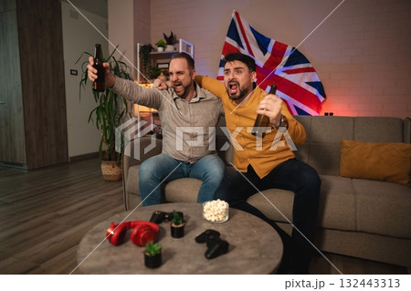 Friends celebrate in a cozy living room while cheering in excitement over a thrilling sports match 132443313